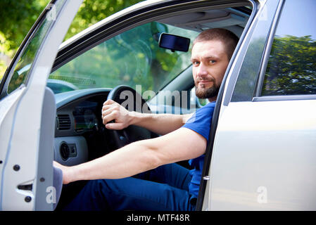 A bearded young man sits in a car with an open door. Stock Photo