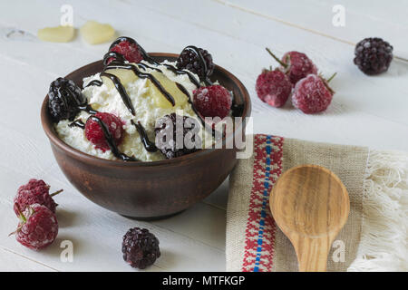 Cottage cheese in a brown ceramic bowl with frozen raspberries and blackberries with authentic flax embroidered napkin and a wooden spoon on a white w Stock Photo