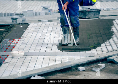 Install paver sidewalk with paving stones, using spacers to achieve consistency between tiles and involves working sand down between the paver joints  Stock Photo
