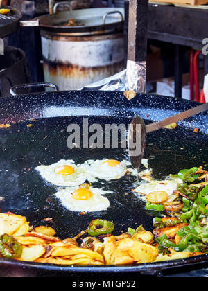 Spanish eggs in progress. Fried eggs with potatoes and peppers to the frying pan. Spanish street food. Stock Photo