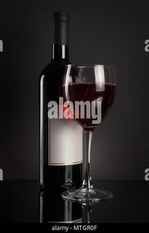Red wine bottle with blank label and full wineglass. On black background Stock Photo