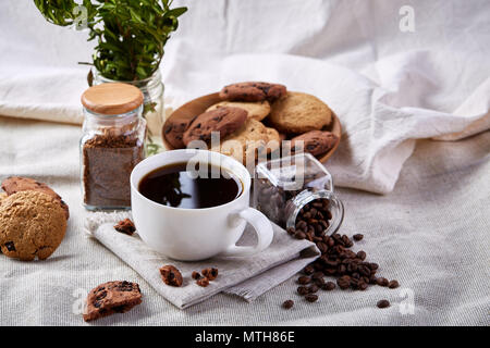 Breakfast still life with coffee cup on napkin, overturned jar with coffee beans, sweet cookies on table covered with white tablecloth, selective focu Stock Photo