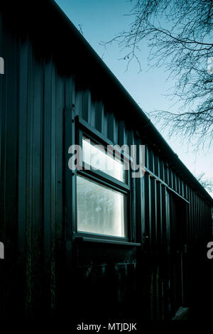 Light coming from a window in a sinister looking building at night. Stock Photo
