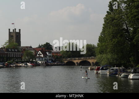 Two people paddlesurfing along the waterway towards the Angel inn and bridge at Henley on Thames Oxfordshire. Stock Photo