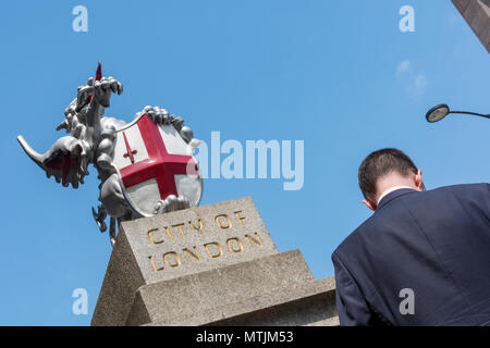 a businessman dressed in a suit next to the griffin sign on london bridge marking the start or the beginning of the city of london financial district. Stock Photo