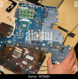 A technician holding a laptop motherboard - mounted on the board is the CPU and 2 sticks of memory (RAM). Stock Photo