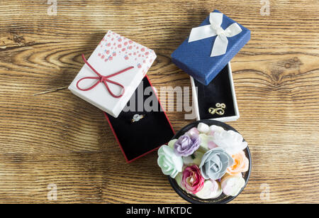 Golden rings lie in a red and blue boxes with many button roses on wooden table Stock Photo
