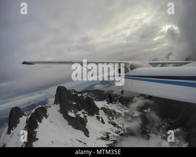 Airplane flying over the beautiful Canadian Mountain Landscape during a cloudy evening. Taken North of Vancouver, British Columbia, Canada. Stock Photo