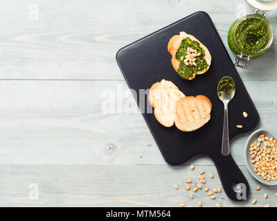 baguette bread with fresh basil pesto sauce on black wooden cutting board over gray wooden table. Top view or flat-lay. Copy space. Stock Photo