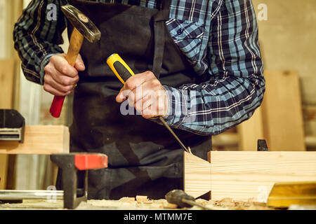 Experienced carpenter in work clothes and small buiness owner working in woodwork workshop,  using chisel for cutting out of wood  in workshop  on the Stock Photo