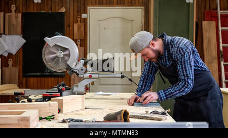 Experienced carpenter in work clothes and small buiness owner working in woodwork workshop, sharpening the tool with whetstone Stock Photo
