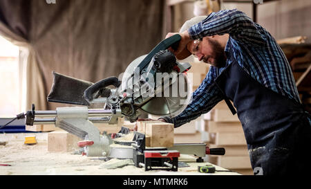 Young man builder carpenter sawing board with circular saw in workshop Stock Photo