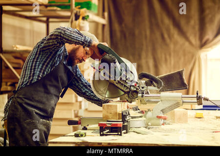 Young man builder carpenter sawing board with circular saw in workshop Stock Photo