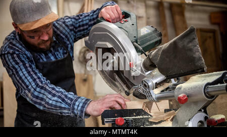 Young man builder carpenter sawing board with circular saw in workshop Stock Photo