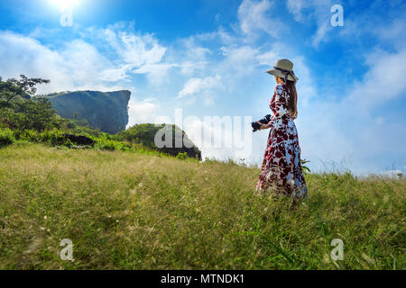 Woman standing on meadow and holding camera at Phu Chi Fa mountains in Chiangrai, Thailand. Travel concept. Stock Photo