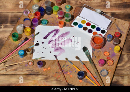 Background image showing interest in watercolor painting and art. A painted sheet of paper, surrounded by brushes, jars of watercolor paint and gouach Stock Photo