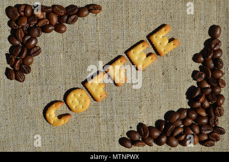 Background of a gray canvas made of old and coarse burlap, on which lies a certain amount of brown coffee beans and the word "coffee", composed of edi Stock Photo