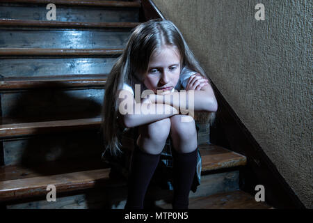 Sad, depressed, unhappy schoolgirl suffering from bullying and abuse feeling lonely and hopeless sitting on stairs with dark light. School isolation,  Stock Photo