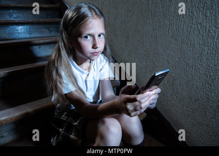 Sad depressed young girl victim of cyberbullying by mobile smart phone sitting on stairs feeling lonely, unhappy, hopeless and abused. Bullied by text Stock Photo