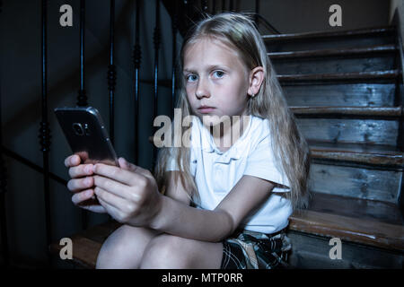 Sad depressed young girl victim of cyberbullying by mobile smart phone sitting on stairs feeling lonely, unhappy, hopeless and abused. Bullied by text Stock Photo