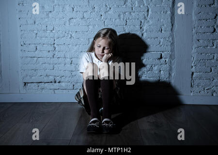 Sad desperate young girl suffering from bulling and harassment felling lonely, unhappy desperate and hopeless sitting against the wall, dark light. Sc Stock Photo