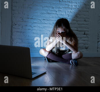 Scared sad girl bullied on line with laptop suffering cyberbullying and harassment feeling desperate and intimidated. Child victim of bullying stalker Stock Photo