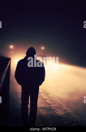 Young man walking down the road on a foggy evening Stock Photo