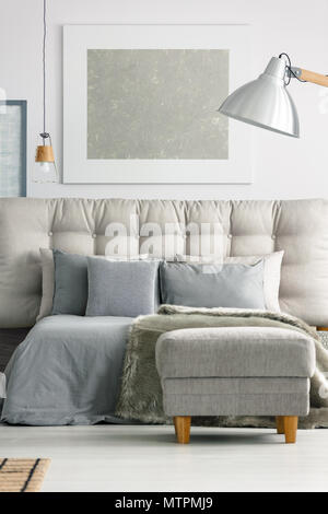 Ottoman by the grey comfortable bed in modern white bedroom Stock Photo