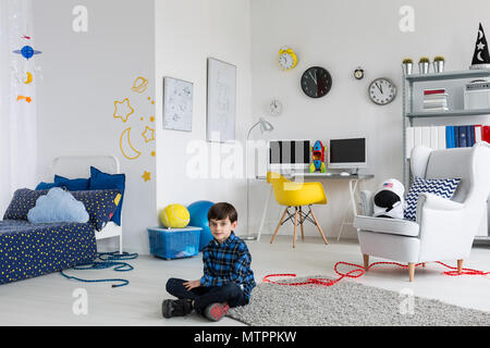 Shot of a little boy sitting on a floor in his space inspired bedroom Stock Photo