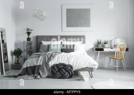 Pile of books placed on the floor next to knot cushion in white room Stock Photo