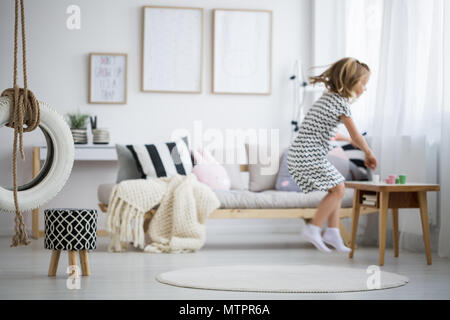 Blonde girl in dress jumping in modern room with swing Stock Photo