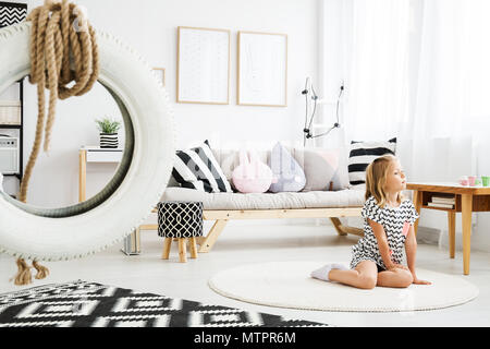 Little blonde girl sitting on floor in trendy scandinavian white room Stock Photo
