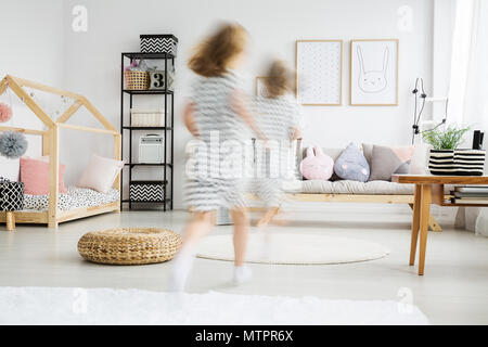 Blurred view of energetic young girl in dress running in trendy room with plush pillows Stock Photo