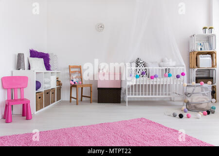 Cute pink and white bedroom designed for little baby girl. By the wall cradle and shelf. On the floor pink carpet Stock Photo