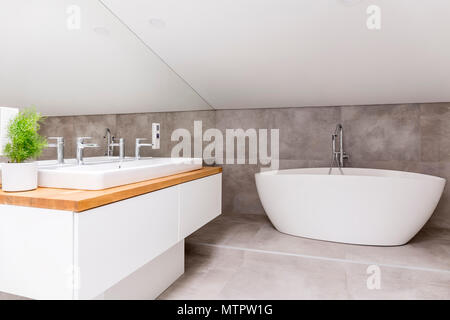 Wooden cupboard with sink and faucet in bathroom with shaped bathtub and mirror Stock Photo