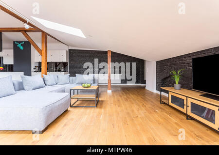 Television on long wooden cupboard in living room with grey couch set and coffee table Stock Photo