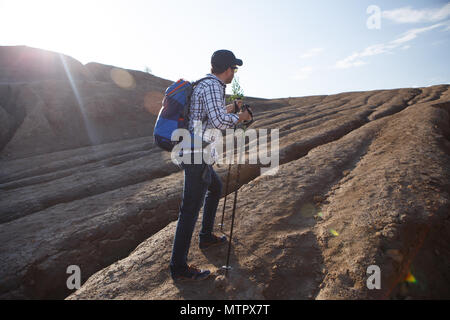 Image of tourist man with walking sticks in mountainous area against sun Stock Photo