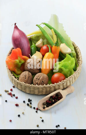 Peppers, walnuts, garlic, green beans and red onion in basket on wooden background Stock Photo