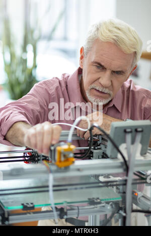 Handsome elderly man adjusting extruder of 3D printer Stock Photo