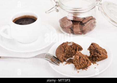Chocolate muffin broken open on a plate, black coffee and pieces of chocolate in a jar. Selective focus Stock Photo