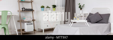 Bedroom with pillows on the bed, white commode and decorations in pastel colours Stock Photo