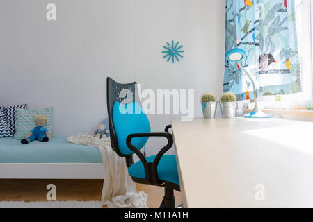 Bright teenager room arranged in white and blue, with large white desk and a swivel chair beside a large window Stock Photo