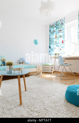 Very bright and spacious teenager room with large fluffy carpet, a coffee table and a blue tuffet Stock Photo