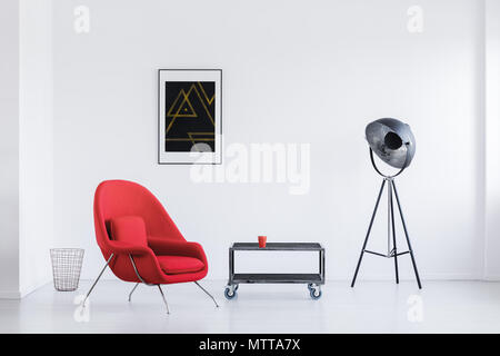 Big studio lamp in day room with red armchair and industrial table with wheels Stock Photo