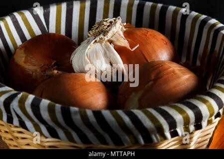 Onions and head of garlic in a wicker basket seen from up close. Rustic style. Horizontal image. Stock Photo