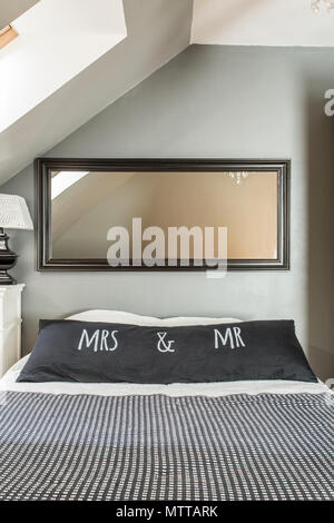 New attic bedroom with mirror, big bed, decorative black and white bedding and cushions Stock Photo