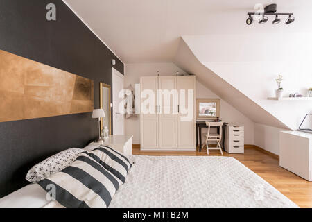 Spacious attic bedroom with black and white walls, large bed and simple white furniture Stock Photo