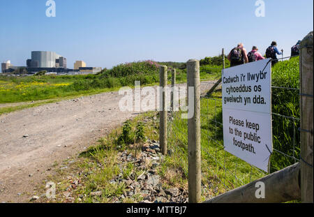 Bilingual sign on Anglesey Coastal Path re-routed around Wylfa Nuclear Power Station with walkers walking in 2018. Cemaes Isle of Anglesey Wales UK Stock Photo