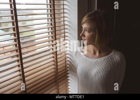Woman looking through window blinds Stock Photo