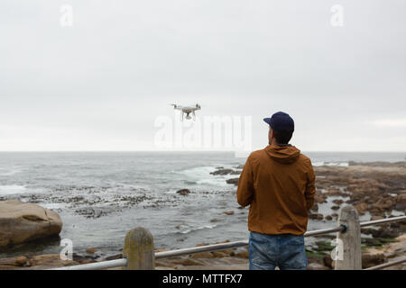 Man operating a flying drone near beach Stock Photo